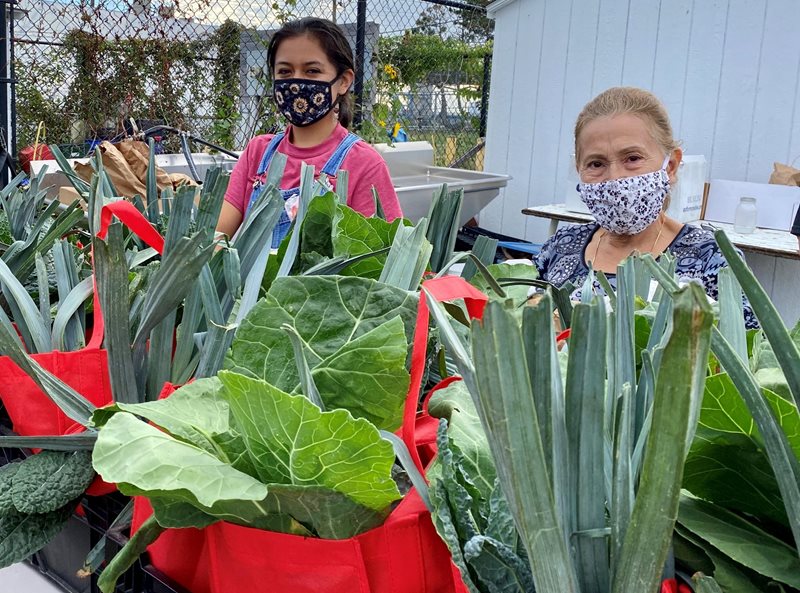 Two women wearing facemasks with bags of fresh produce