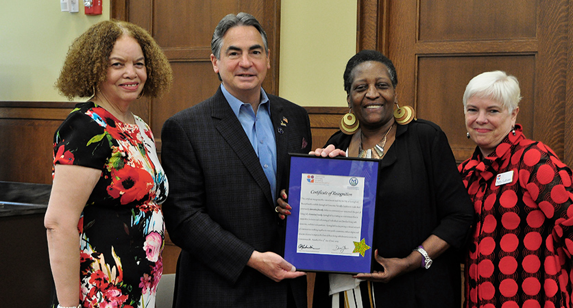 Three women and one man posing for picture holding up a document